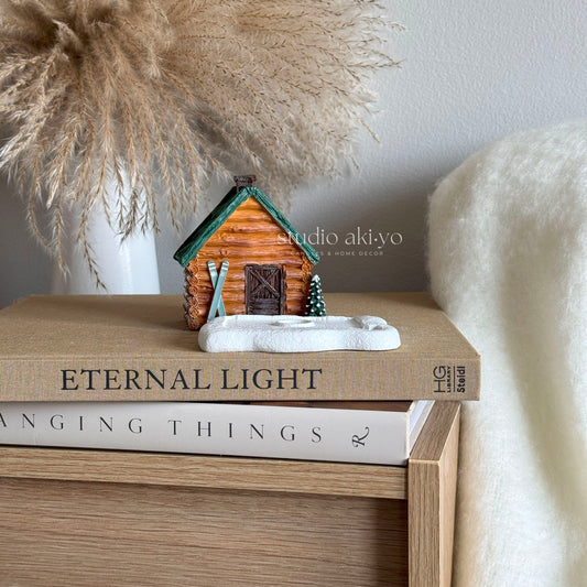 Small wooden cabin figurine on a stack of books with decorative elements.