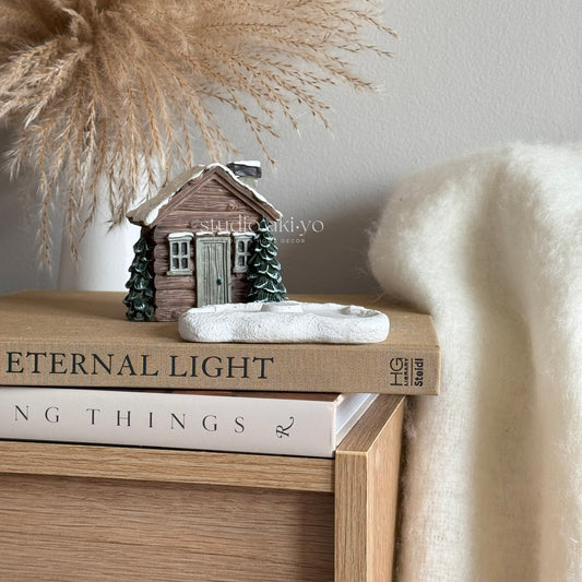 Winter Log cabin incense cone holder on top of books with a soft background