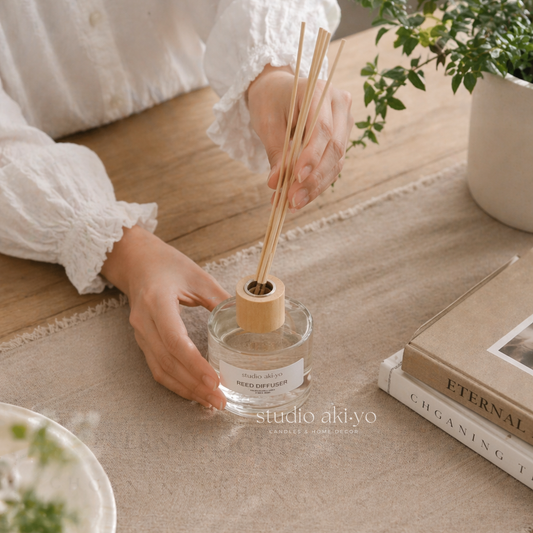 Person holding a diffuser with reeds on a wooden surface, with 'studio akiyo' branding.