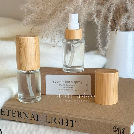 Two Studio Akiyo room linen spray bottles with luxurious bamboo caps on a book titled 'Eternal Light'.