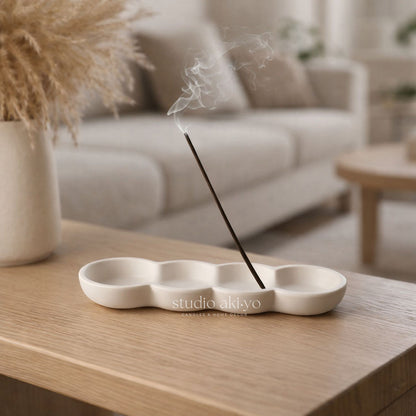 Incense stick burning on a white ceramic holder with 'studio akiyo' branding, placed on a wooden table.