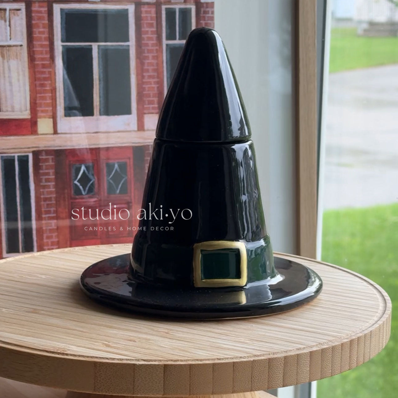 Black hat-shaped container with a gold buckle on a wooden surface, branded 'studio akiyo'.