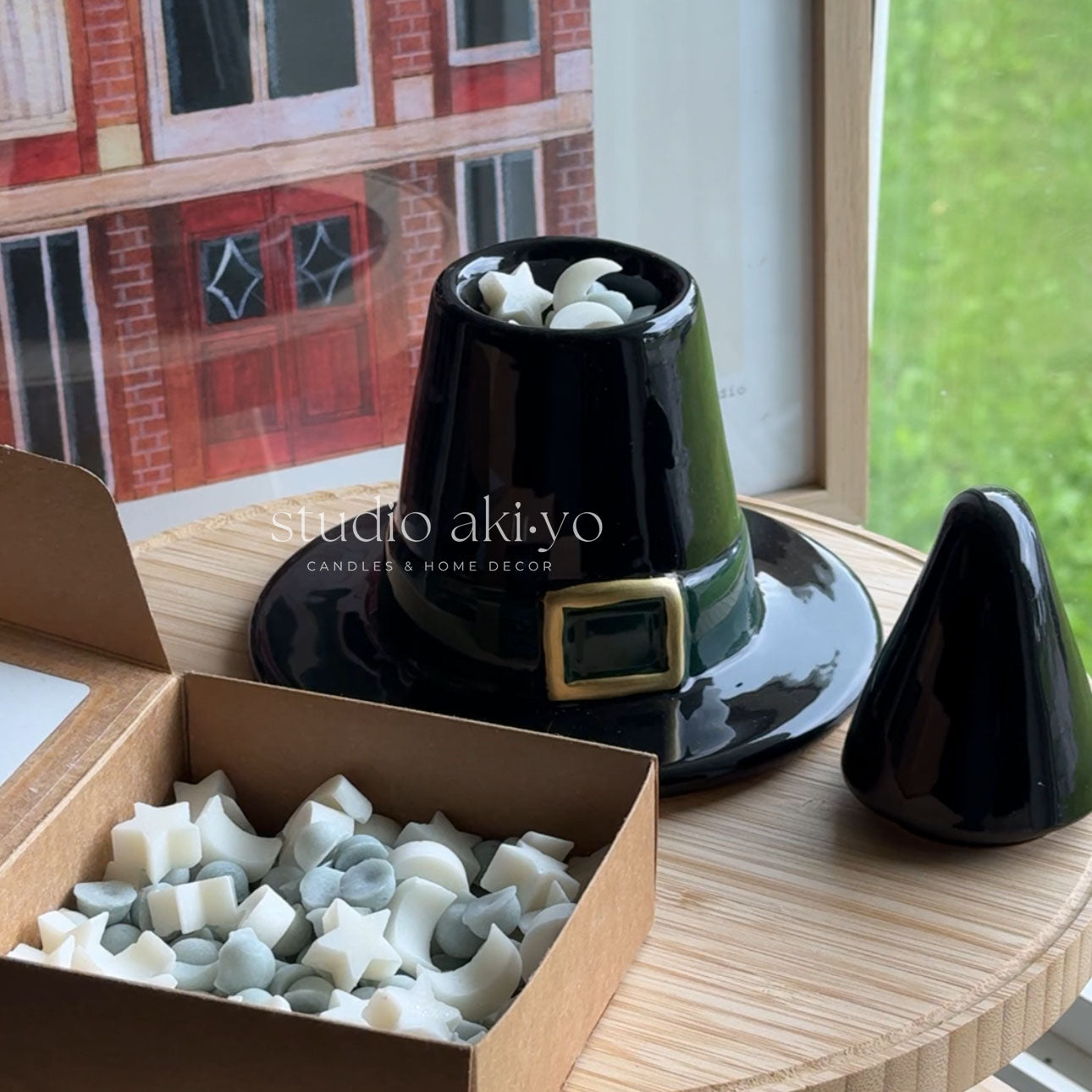 Black decorative item with a gold buckle on a wooden surface, next to a box of candle wicks.