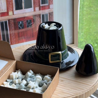 Black decorative item with a gold buckle on a wooden surface, next to a box of candle wicks.