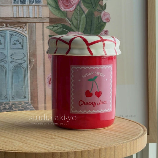Red jar labeled 'Sugar Sweet Cherry Jam' on a wooden surface with floral background