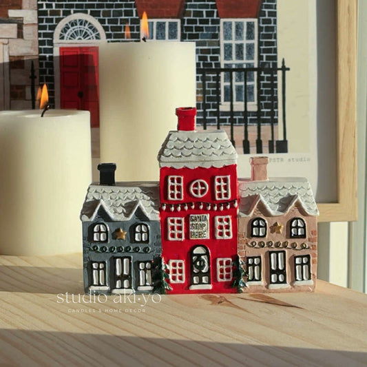 Decorative house models with a candle on a wooden surface, featuring 'studio akiyo' branding.