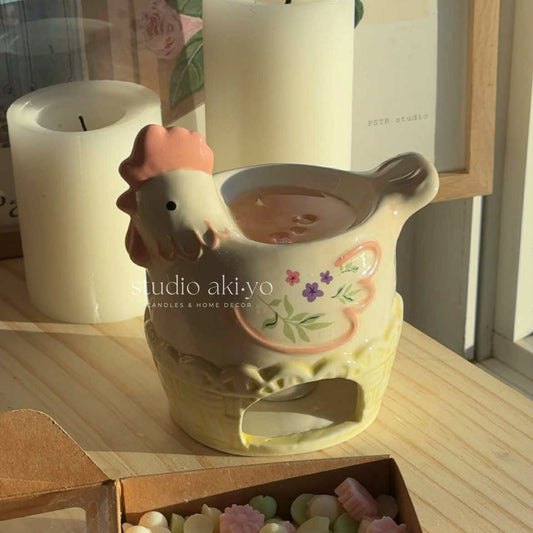 Ceramic chicken-shaped wax melt burner on a stack of books with decorative elements.