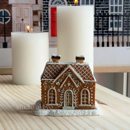 Decorative gingerbread house on a table with candles in the background