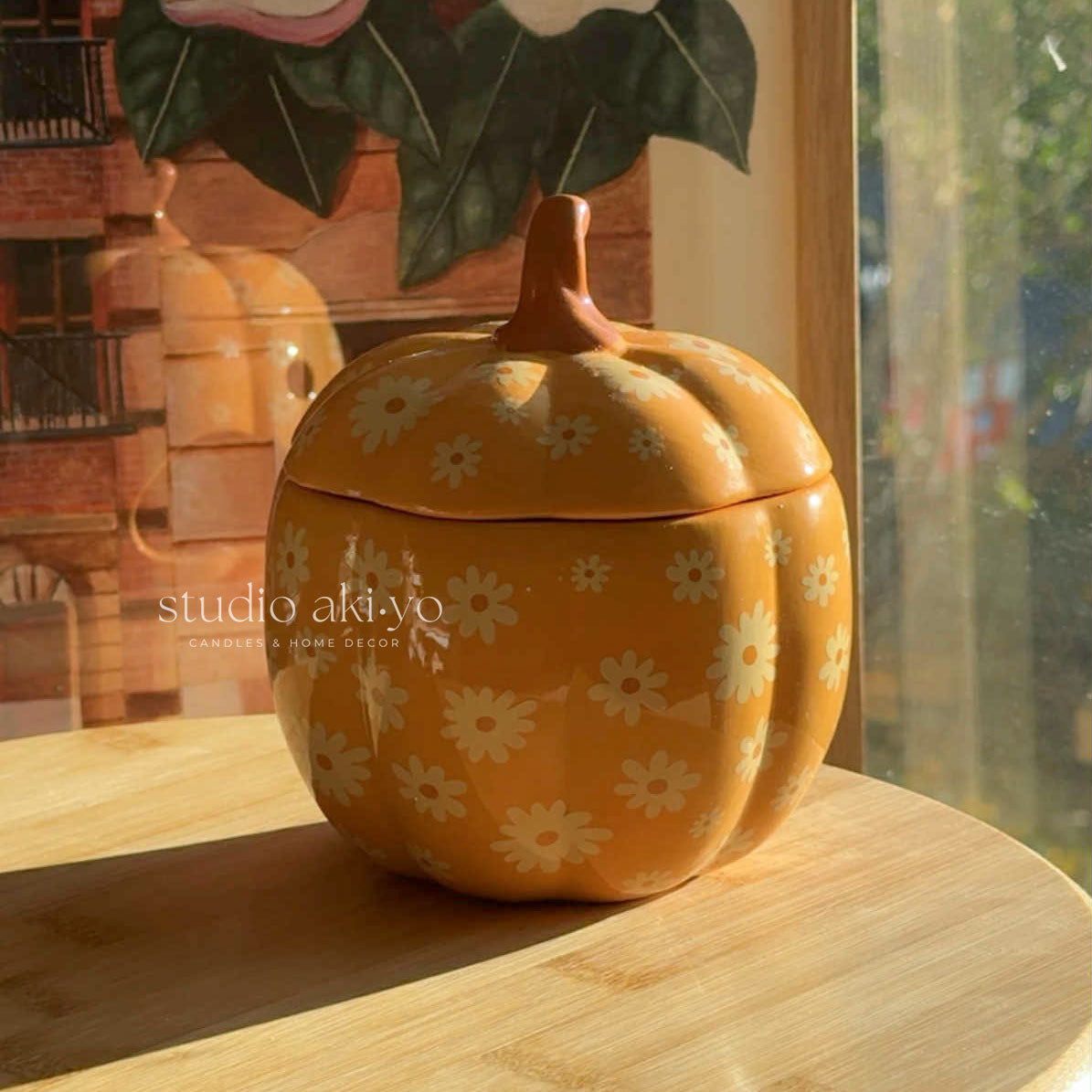 Yellow pumpkin-shaped cookie jar with floral patterns on a wooden surface, brand 'studio akiyo' visible.