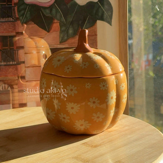 Yellow pumpkin-shaped cookie jar with floral patterns on a wooden surface, brand 'studio akiyo' visible.