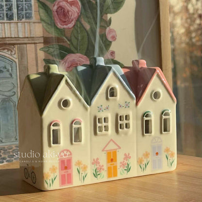 Ceramic pastel village house incense cone with smoke rising from the chimney. 