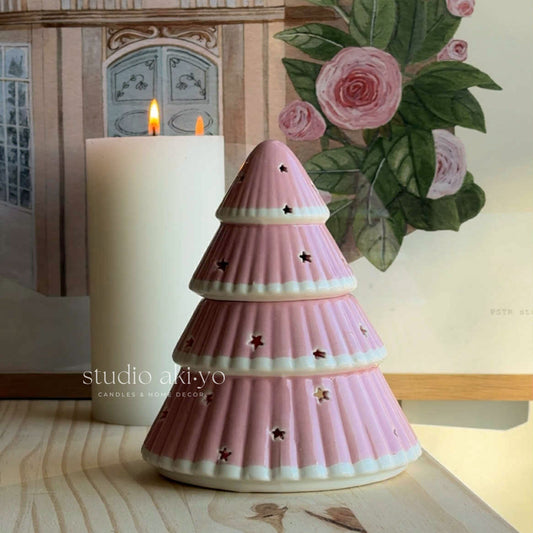 Pink ceramic Christmas tree decoration with a candle on a wooden surface, featuring the brand 'studio akiyo'.