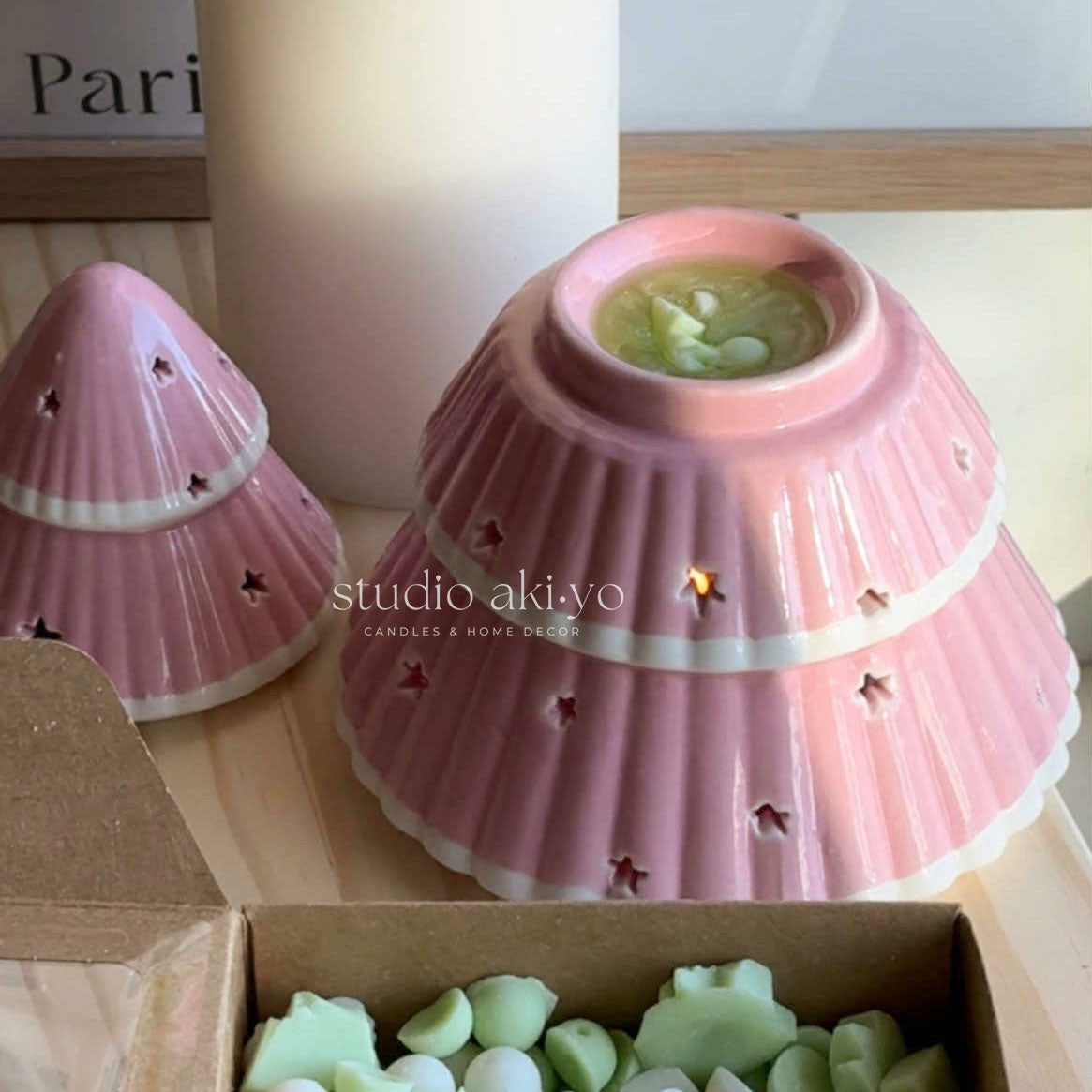 Pink ceramic shell-shaped candle with green wax inside, placed on a wooden surface.