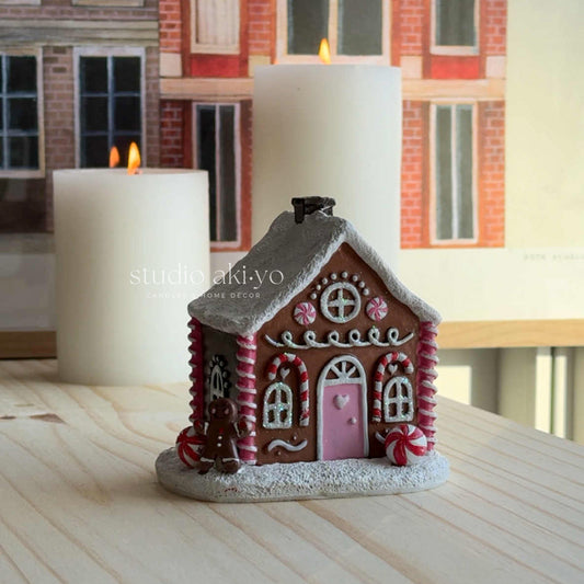 Decorative gingerbread house candle on a wooden surface with candles in the background.