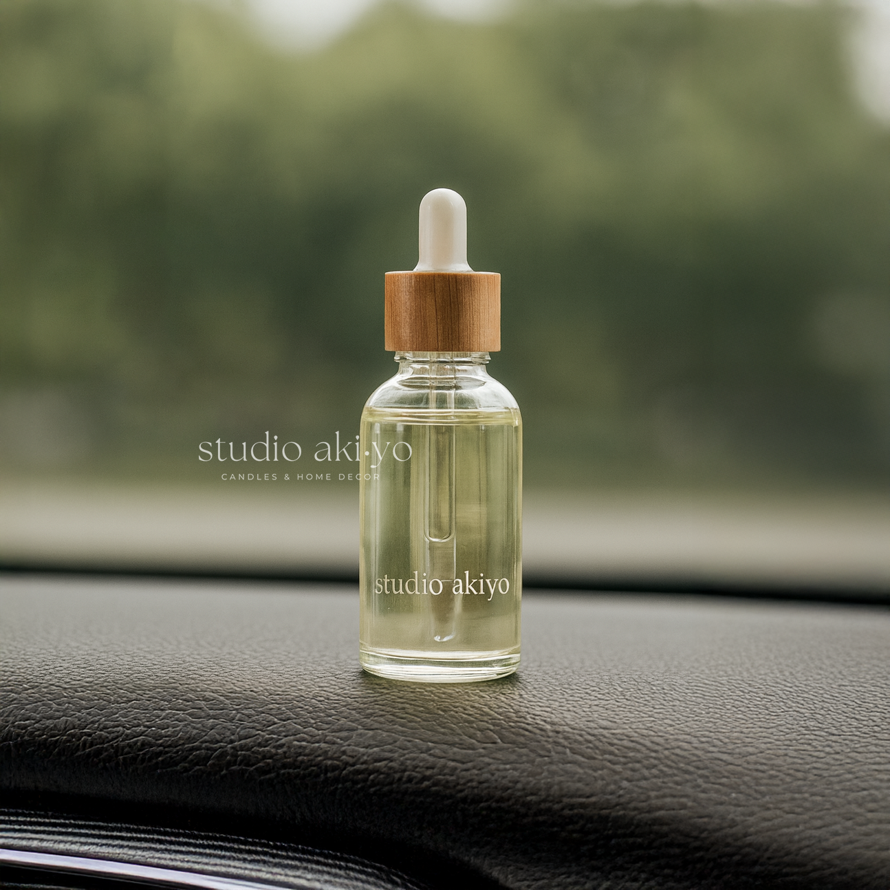 Hanging car diffuser refill in a clear glass dropper bottle with wooden cap on a car dashboard, featuring 'studio akiyo' branding.