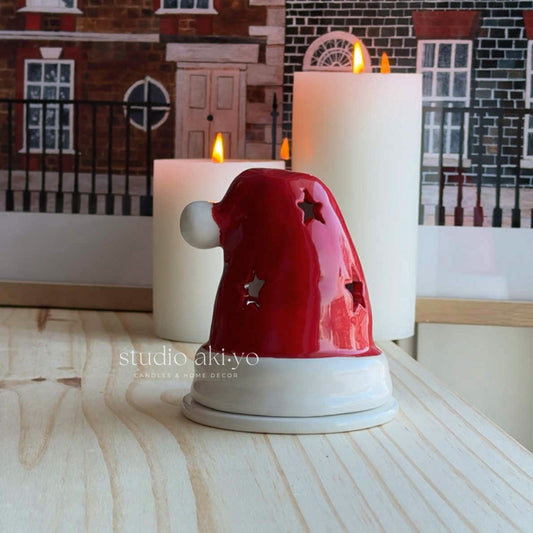 Red Santa hat candle holder with lit candles on a wooden surface, branded 'studio akiyo'.