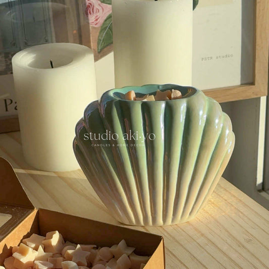 Shell-shaped wax melt burner on books with decorative plant and neutral background