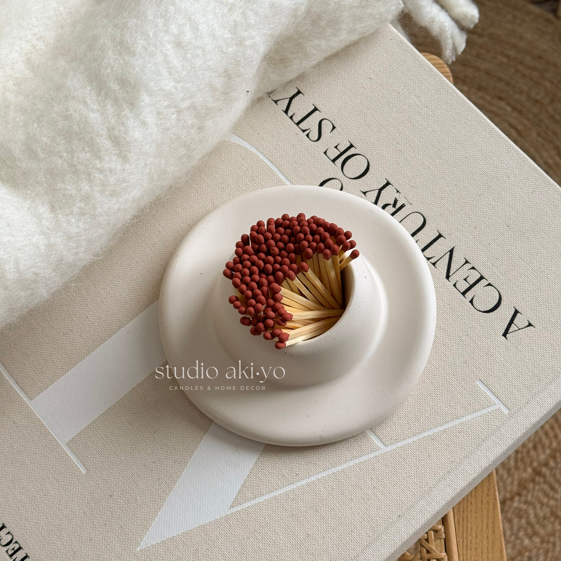 White ceramic container with matchsticks on a textured surface with 'studio akiyo' branding.
