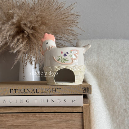 Ceramic chicken-shaped planter on a stack of books with decorative elements.