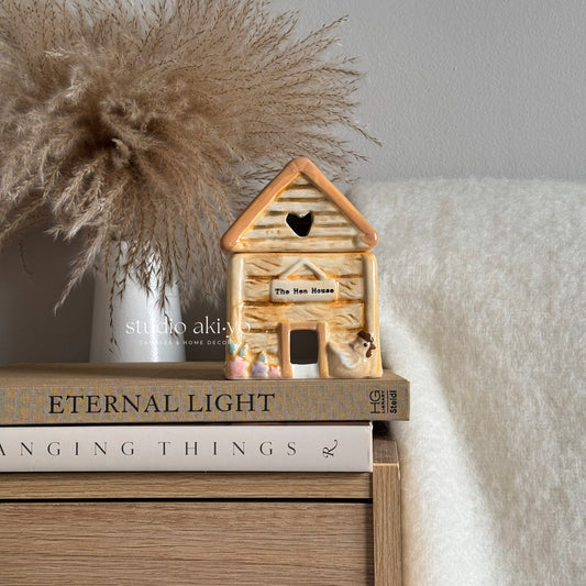 Hen house chicken coop wax melt burner on a stack of books with decorative elements.