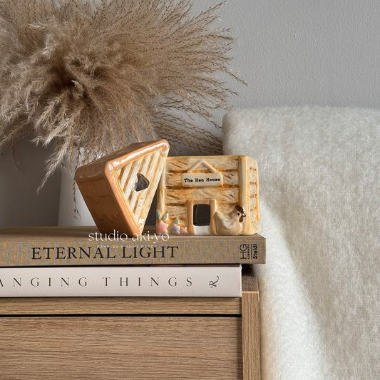 Pastel hen house chicken coop wax melt burner on a stack of books with decorative elements.