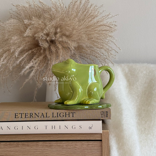 Green ceramic pitcher on books with decorative pampas grass and a white blanket in the background