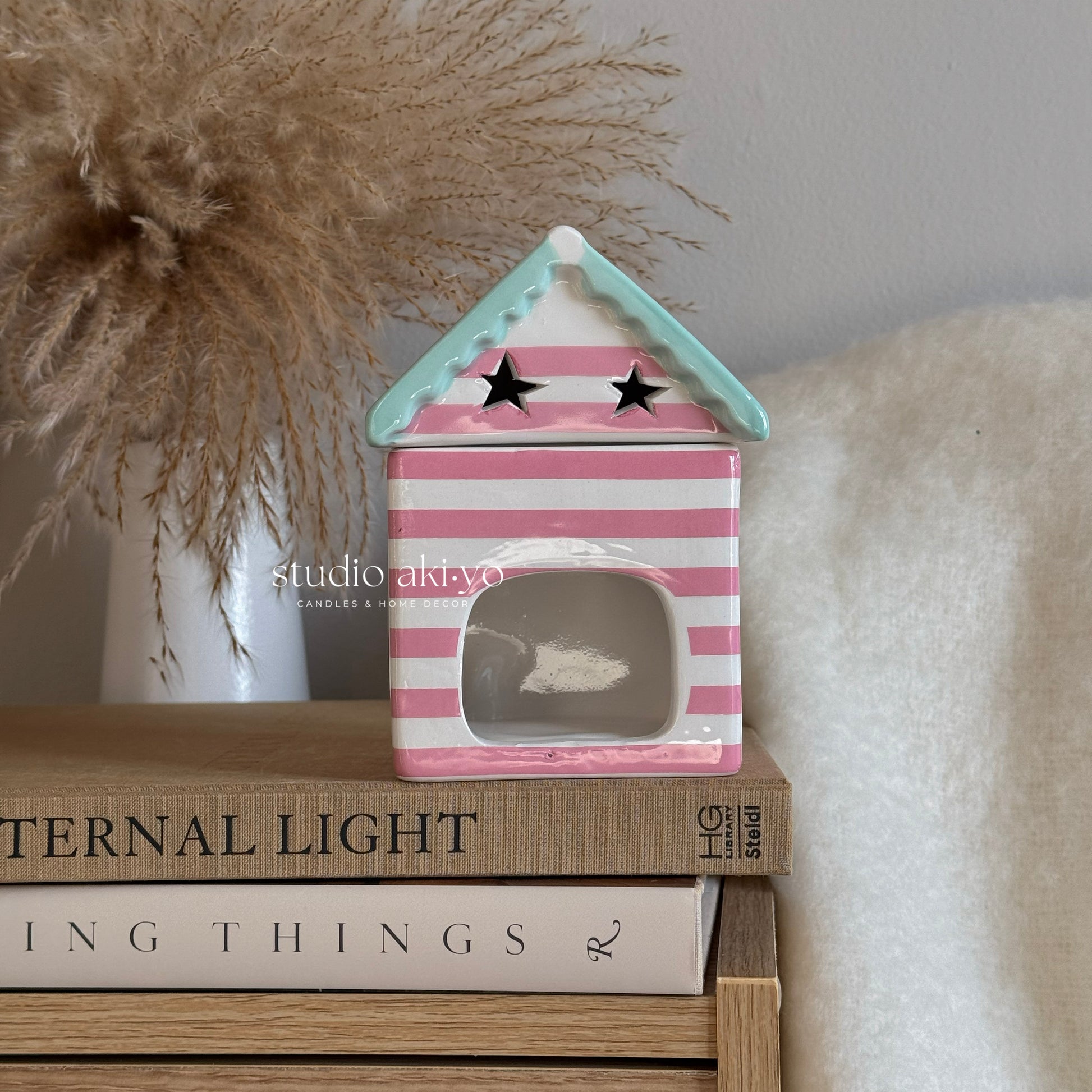 Pink and white striped house-shaped lantern on books with 'studio akiko' branding