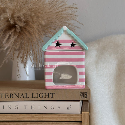 Pink and white striped house-shaped lantern on books with 'studio akiko' branding