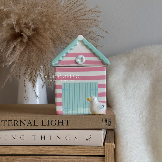 Decorative beach hut with striped pattern on a stack of books, featuring 'studio aidyo' branding.