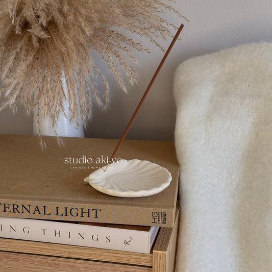 Incense stick on a small white dish with books and decorative elements in the background