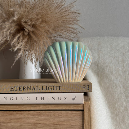 Shell-shaped wax melt burner on books with decorative plant and neutral background