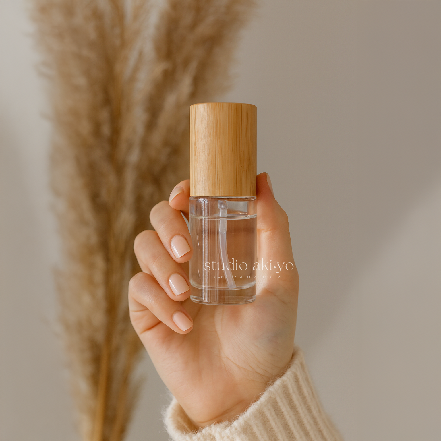 Hand holding studio akiyo room linen spray bottle on a soft, textured surface with a blurred background