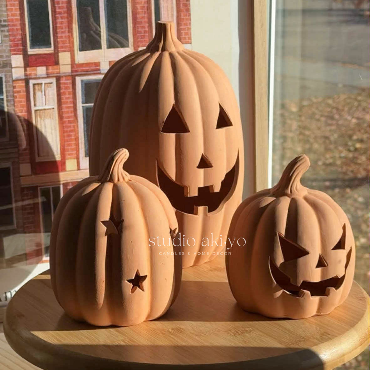 Three terracotta pumpkins with carved faces on a wooden surface.