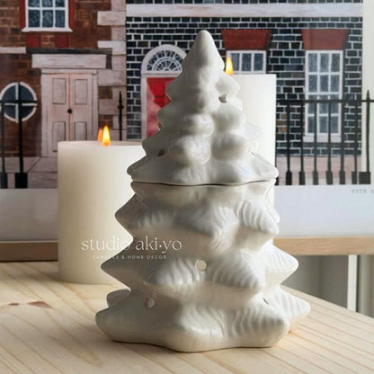 White ceramic tree-shaped diffuser with a candle in front of a decorative fireplace.