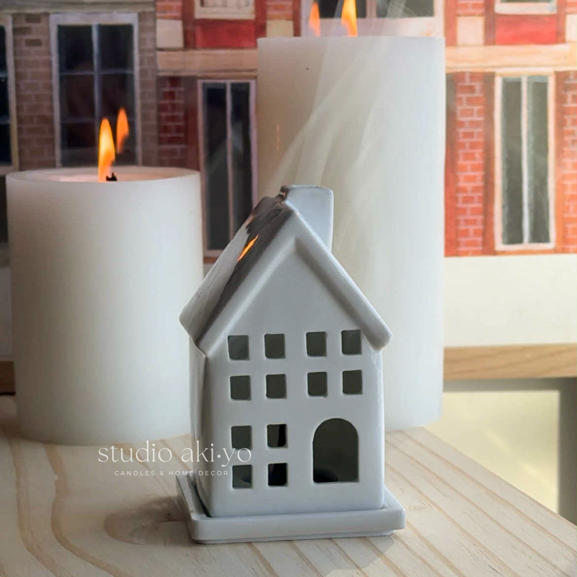 White house-shaped incense cone holder with a lit candle on a wooden surface.