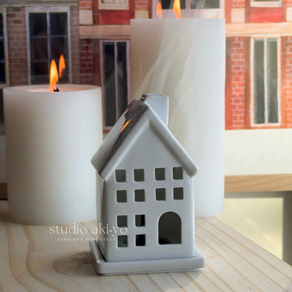 White house-shaped incense cone holder with a lit candle on a wooden surface.