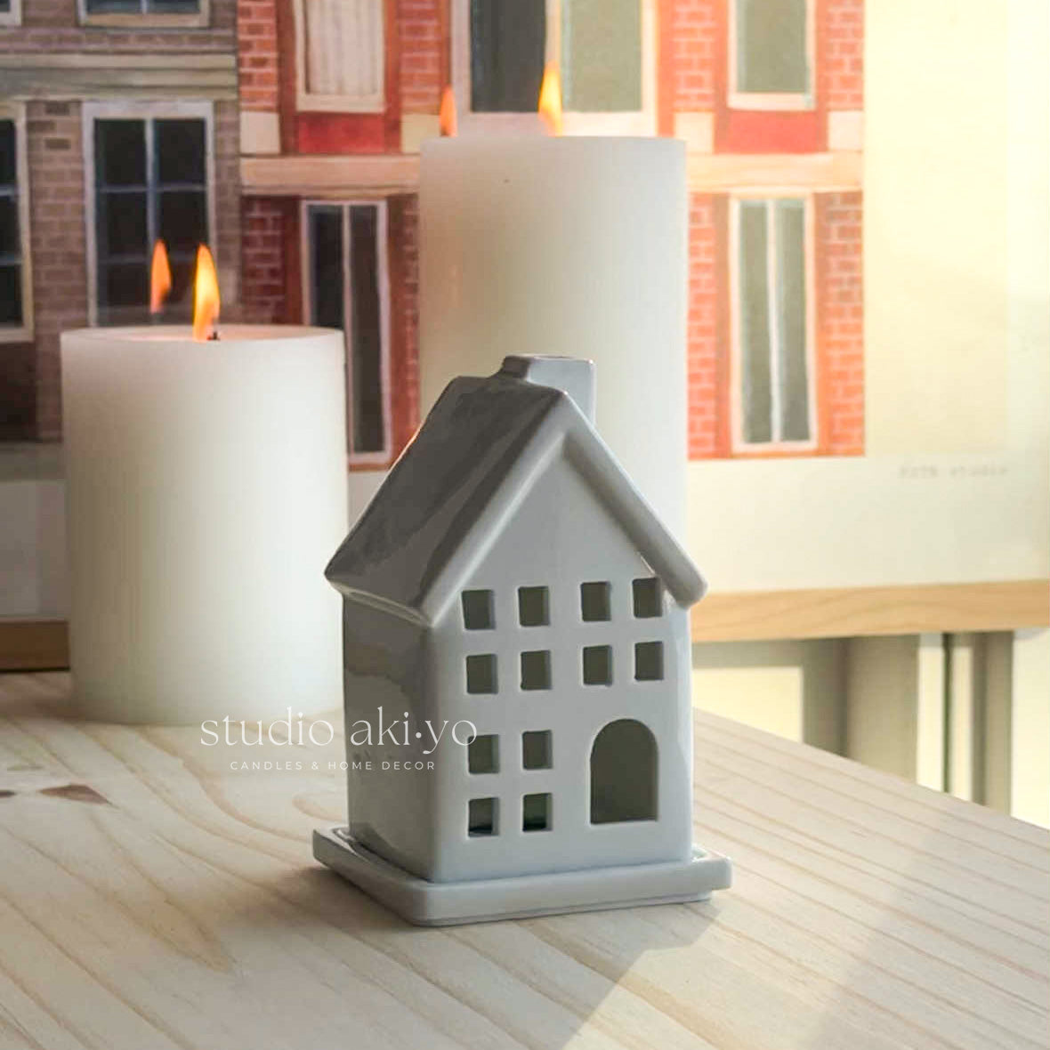 White house-shaped incense cone holder with a lit candle on a wooden surface.